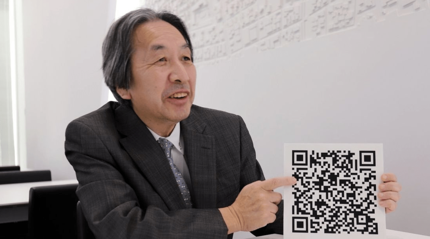 Photo de Masahiro Hara, inventeur du QR code, montrant fièrement un QR code, utilisée pour illustrer l'œuvre LEGO de qargo en hommage à son innovation technologique.