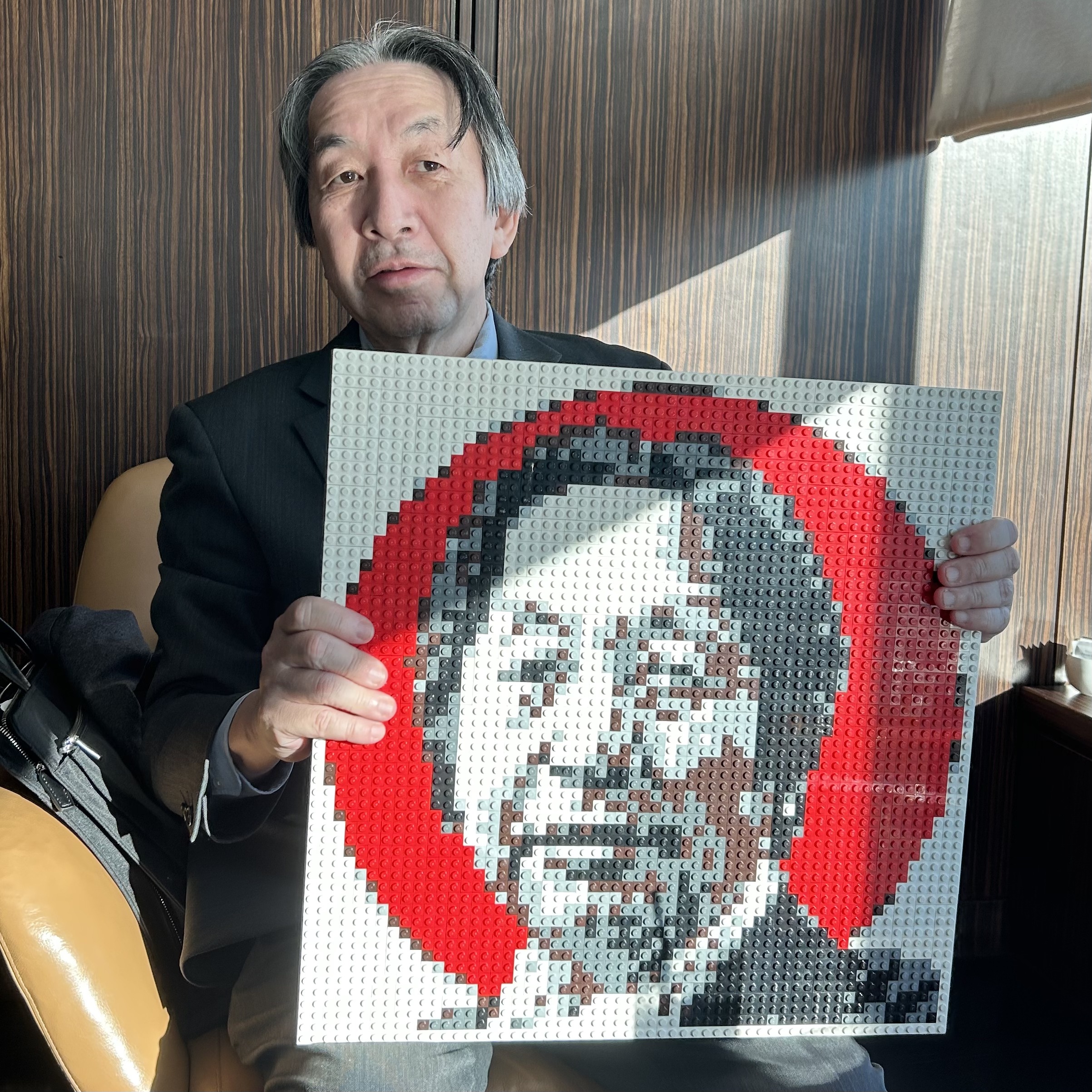 Masahiro Hara, l'ingénieur japonais créateur du QR Code, assis et présentant l'œuvre d'art 'Qargo', un portrait de lui-même fait en Lego.