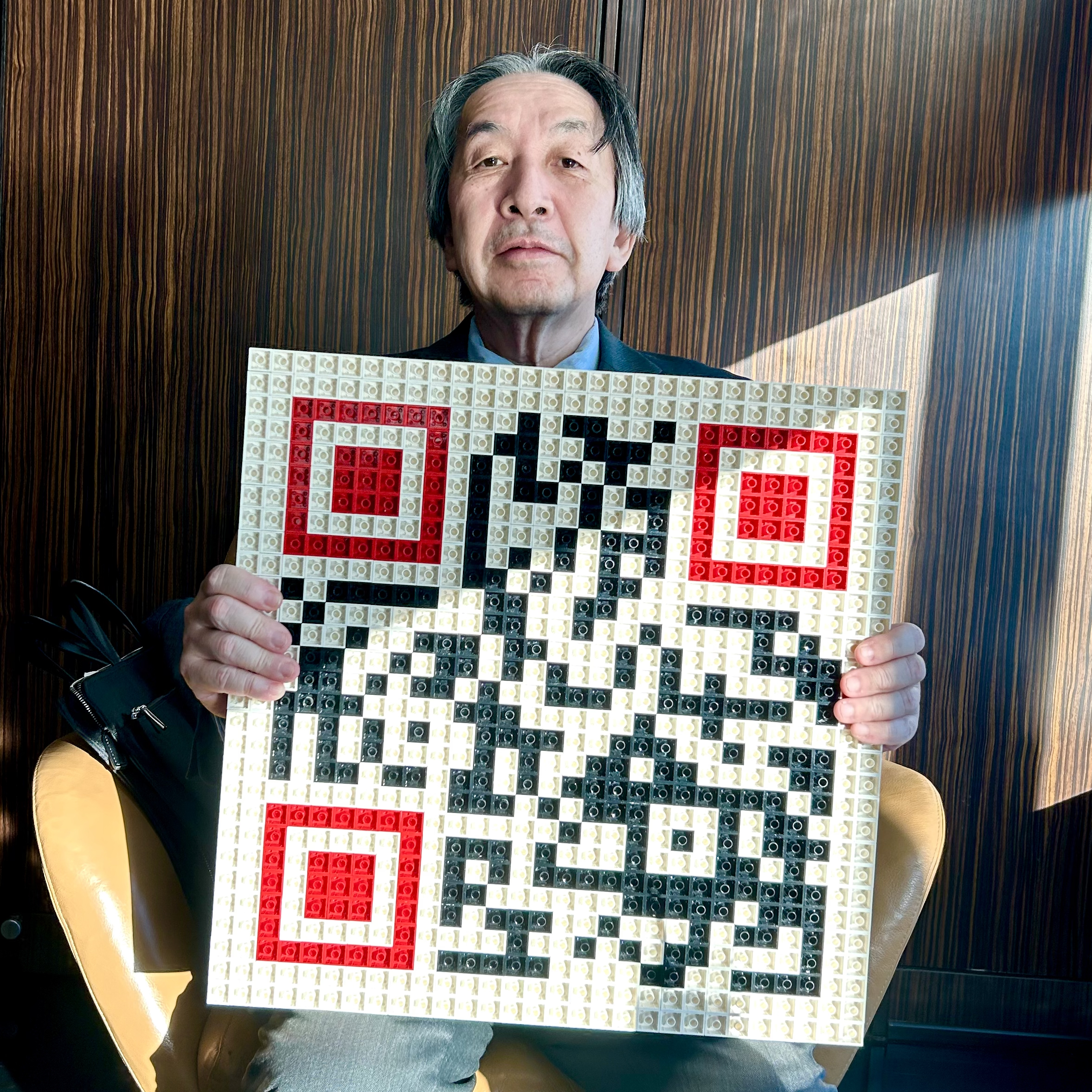 Masahiro Hara, l'ingénieur japonais créateur du QR Code, assis et présentant l'œuvre d'art 'Qargo', un QR code fait en Lego.